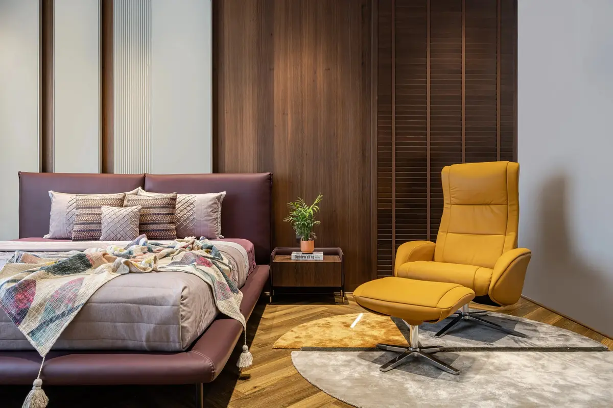 Bedroom with a plum upholstered bed, timber slatted wall and a yellow leather recliner