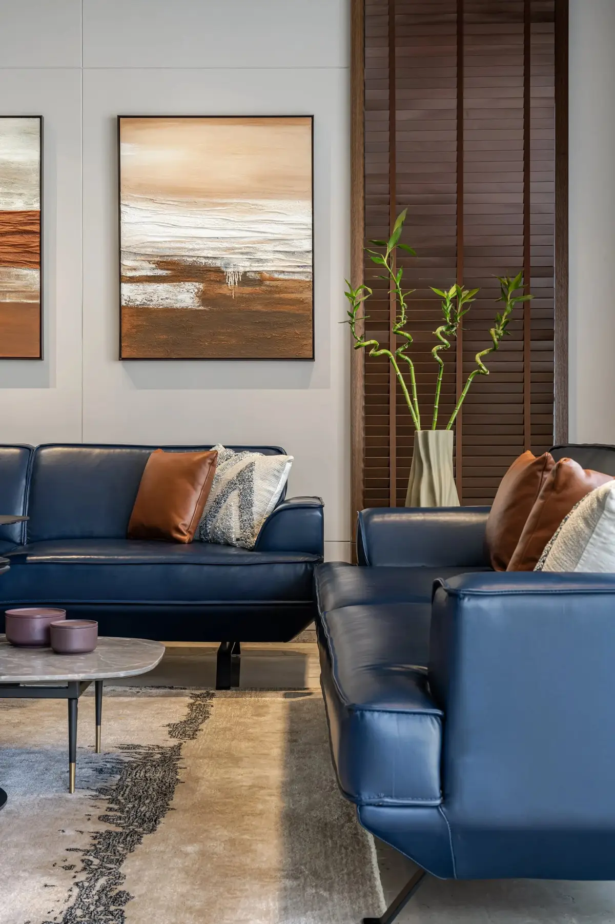 Blue leather sofas with cushions and an artwork pair against a pale wall