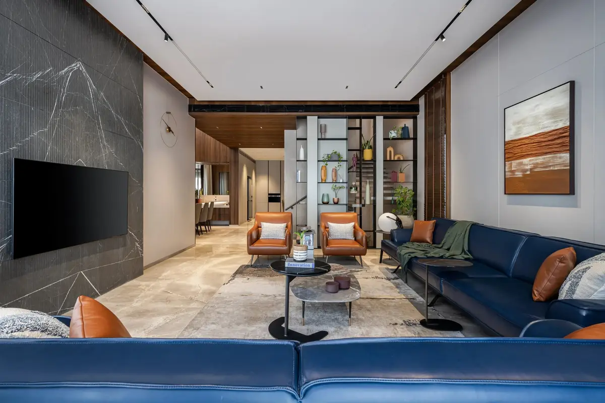 Living area with a veined marble TV wall, blue leather seating and the dining space beyond